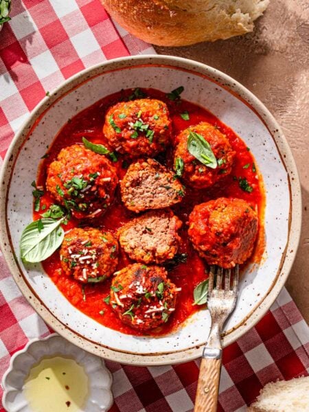 Vegan meatballs simmered in marinara sauce, garnished with fresh basil and parsley, served in a shallow bowl with crusty bread on the side.