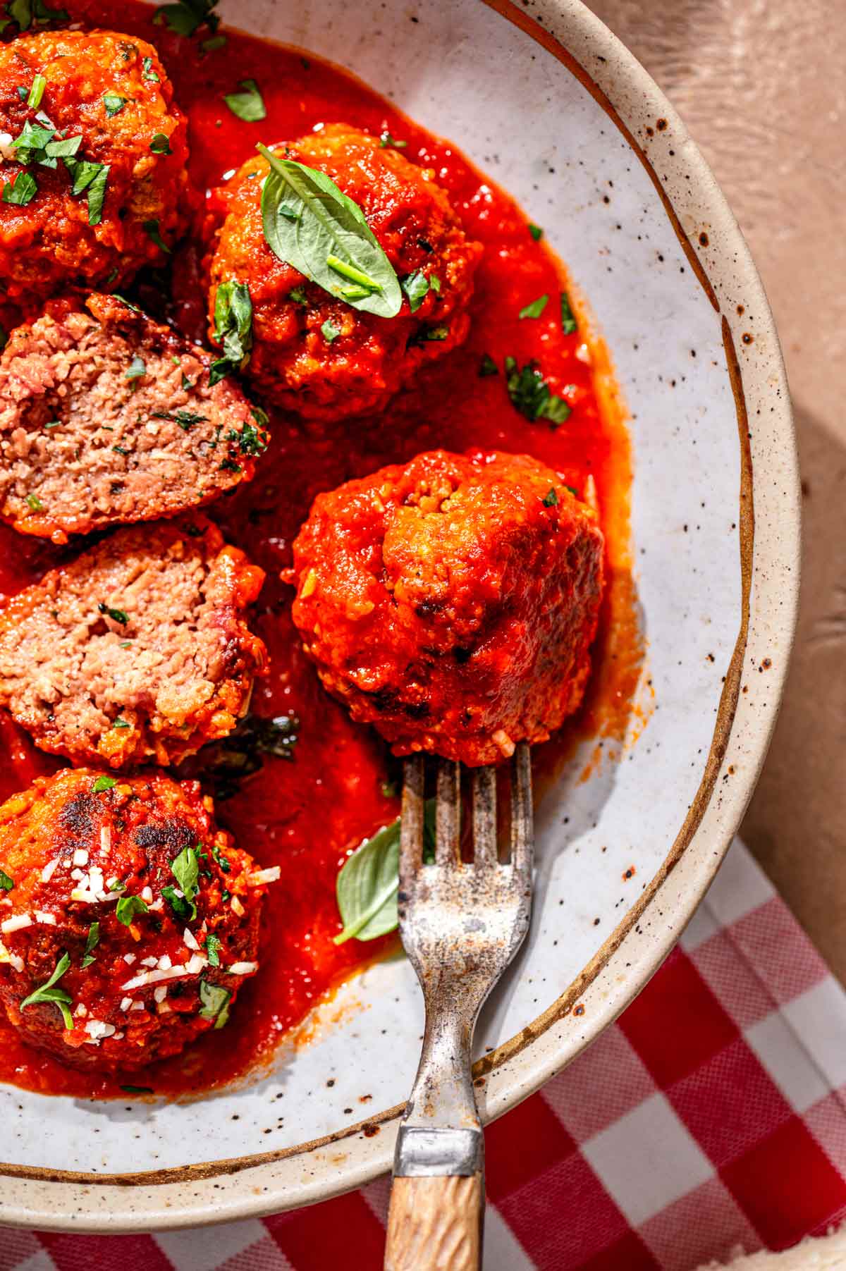 Vegan meatballs coated in tomato sauce with a fork lifting one meatball, showing a firm yet juicy interior.