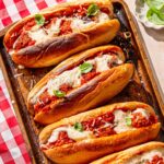 a tray with four vegan meatball subs stuffed with tvp meatballs and covered in a dairy-free cheese sauce.