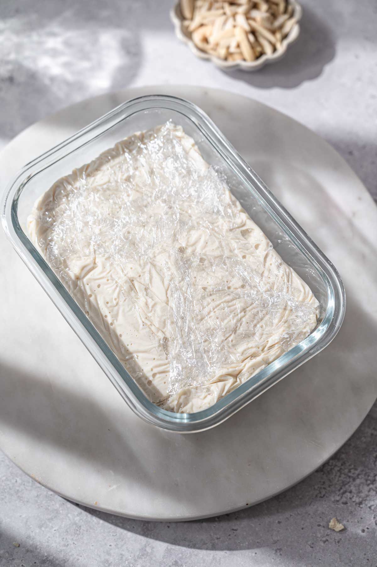 the dairy free feta mixture in a glass container with plastic wrap.