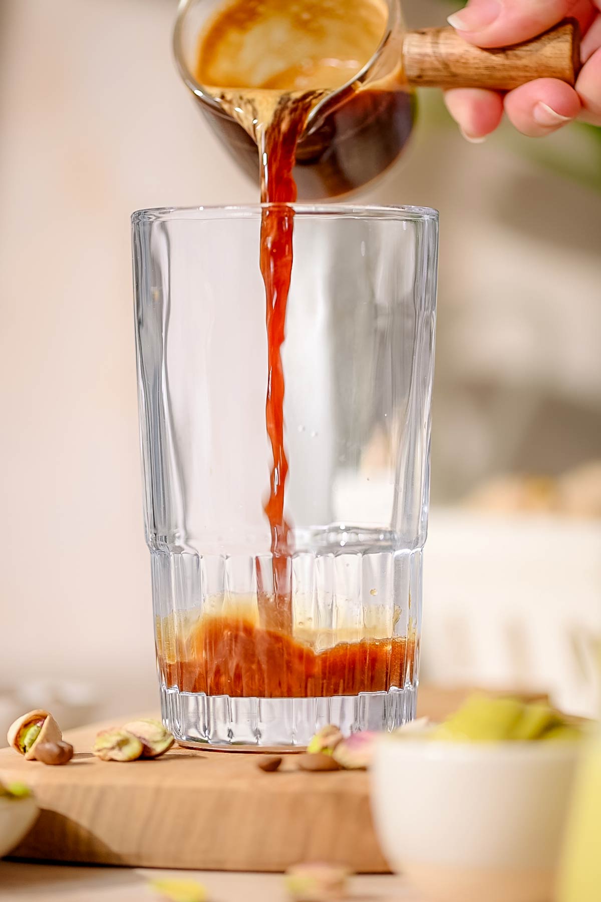 a hand pouring espresso into a tall glass.