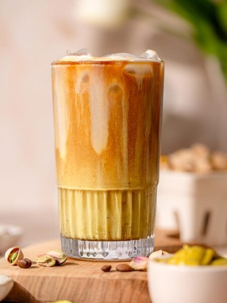 iced pistachio latte in a tall glass with a bowl on pistachio cream in front.