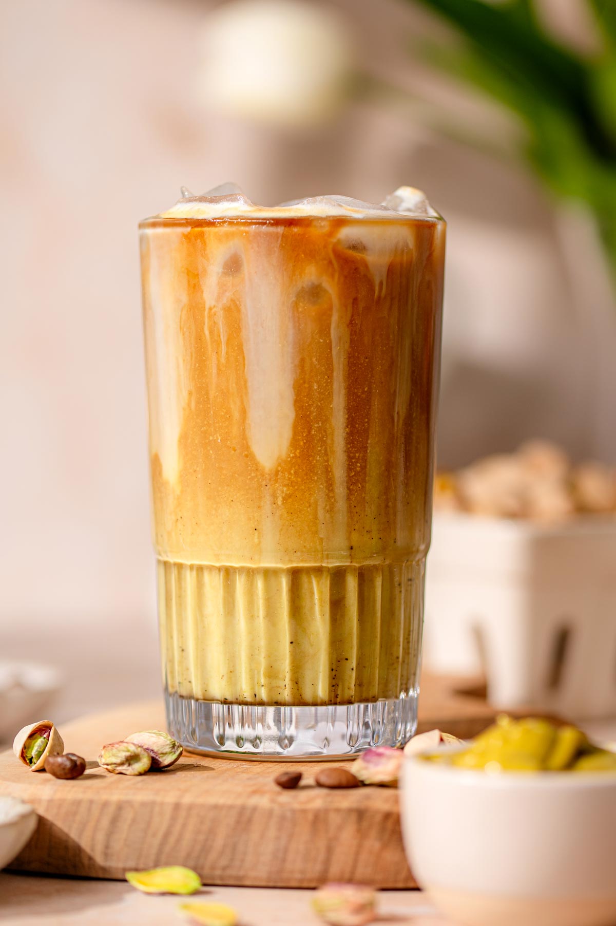 iced pistachio latte in a tall glass with a bowl on pistachio cream in front.