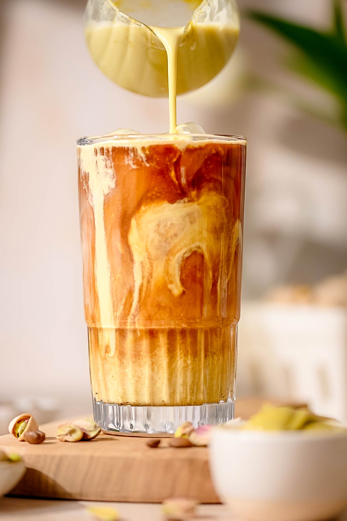 a pitcher of pistachio milk pouring into a glass with espresso and ice.