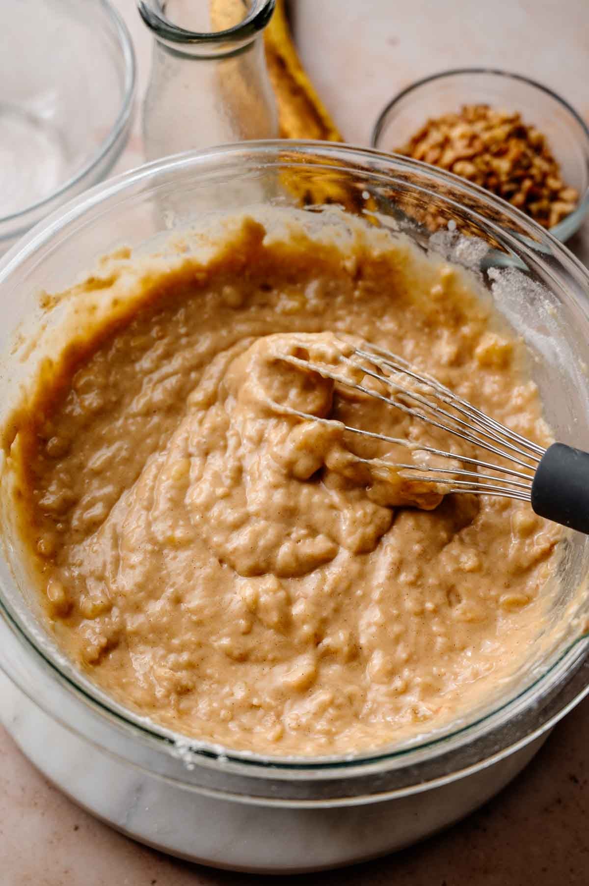 a whisk mixing the vegan banana bread batter in a large glass bowl.