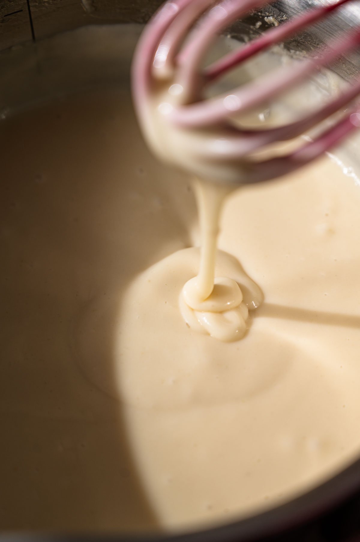 the thickened vegan cheese sauce drizzling off a whisk into a pot.