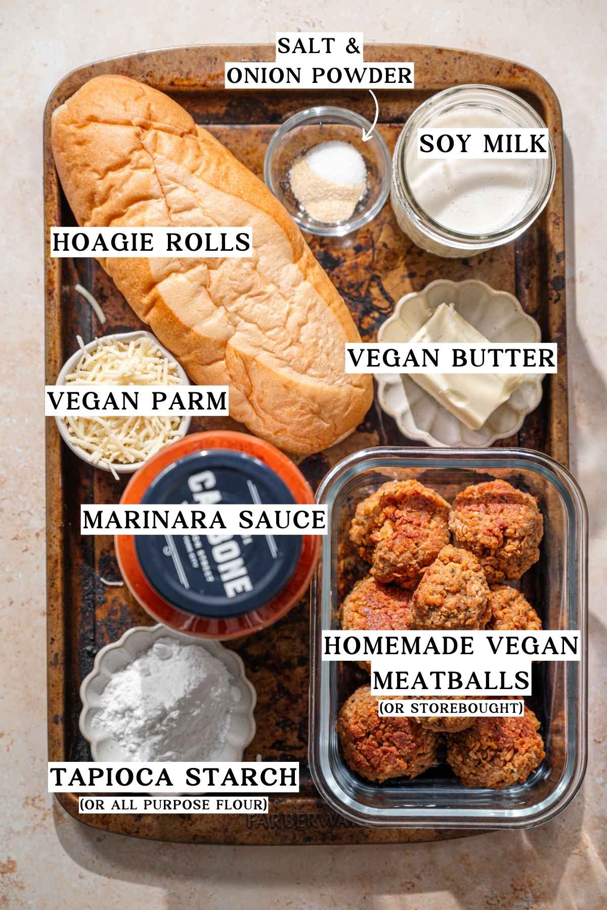ingredients like homemade vegan meatballs, marinara sauce, hoagie rolls, and vegan cheese on a metal baking pan.