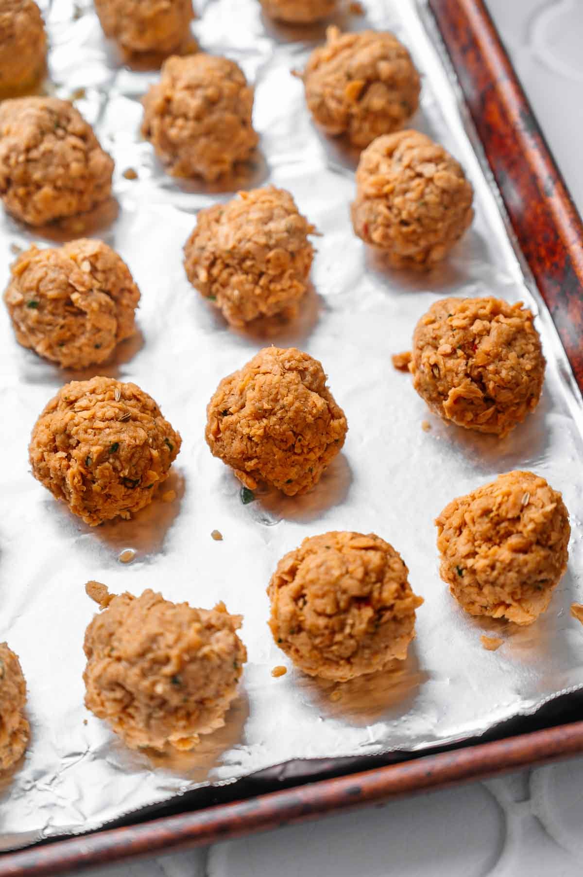 Uncooked vegan meatballs shaped and arranged on a foil-lined baking sheet before baking.