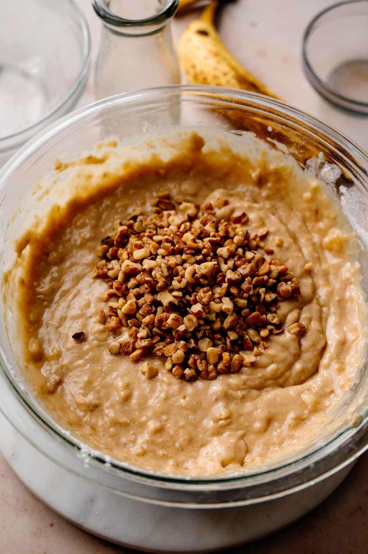 chopped walnuts on top of the eggless banana bread batter in a large glass bowl.