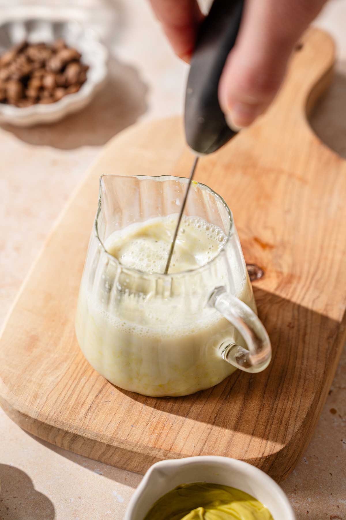 a hand whisking pistachio cream into a small pitcher of oat milk.