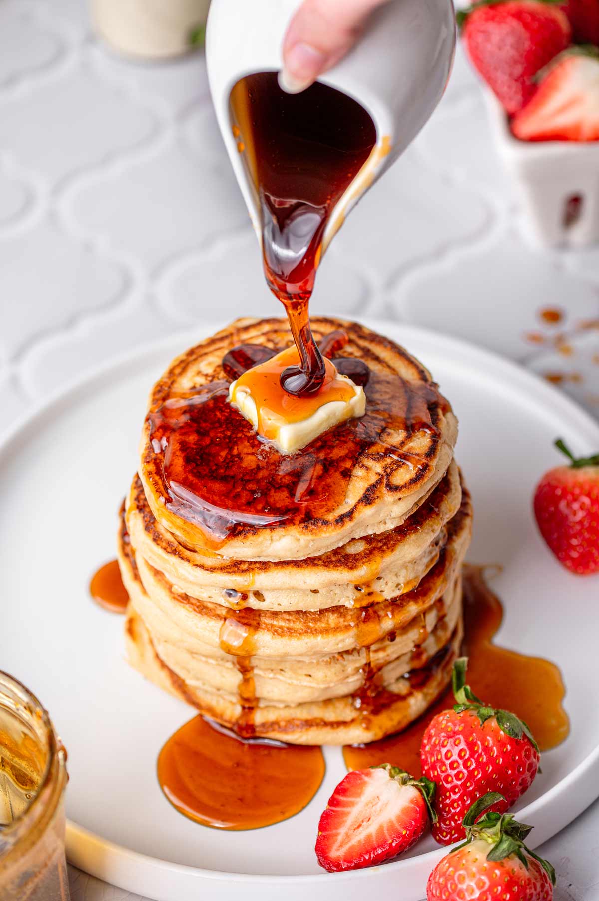 a stack of vegan pancakes with syrup being poured on top.
