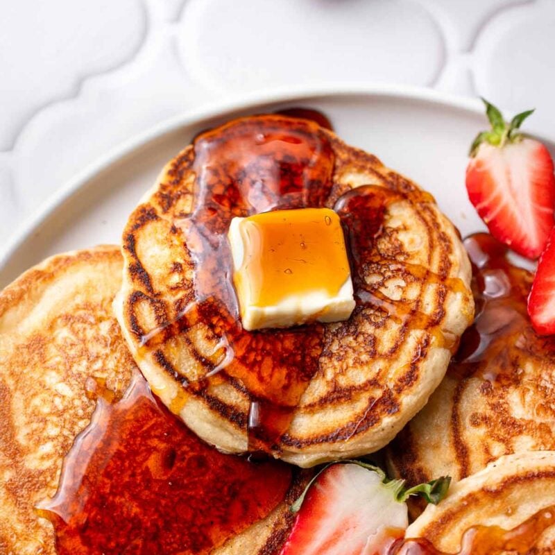 the very best fluffy vegan pancakes on a plate with syrup and dairy-free butter.