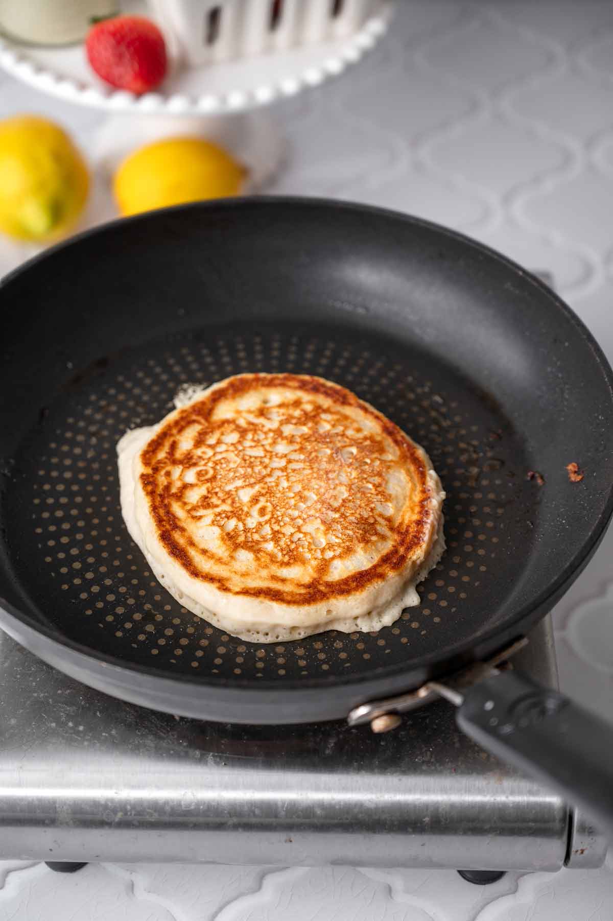 the flipped fluffy vegan pancake on a nonstick pan revealing the crispy fried textured.