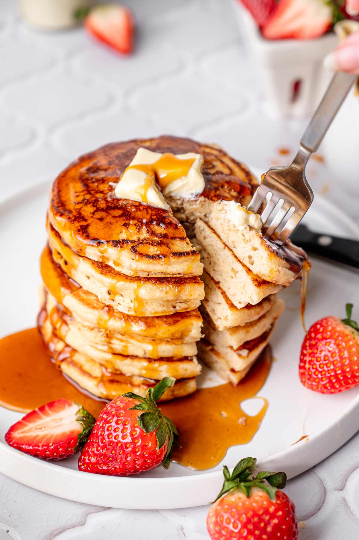 a stack of vegan pancakes with a bite cut out revealing the fluffy texture.