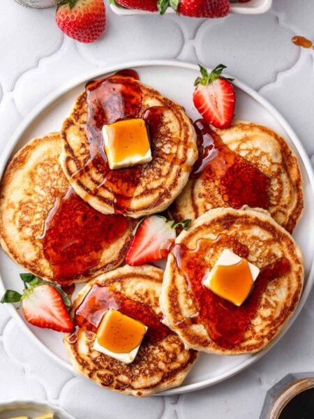 a platter with pan fried vegan pancakes made with dairy-free buttermilk topped syrup and butter pats.