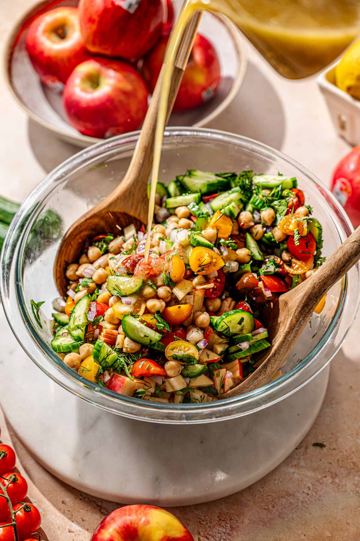lemon dressing being poured on top of the tossed vegan dense bean salad with cucumbers and tomatoes.