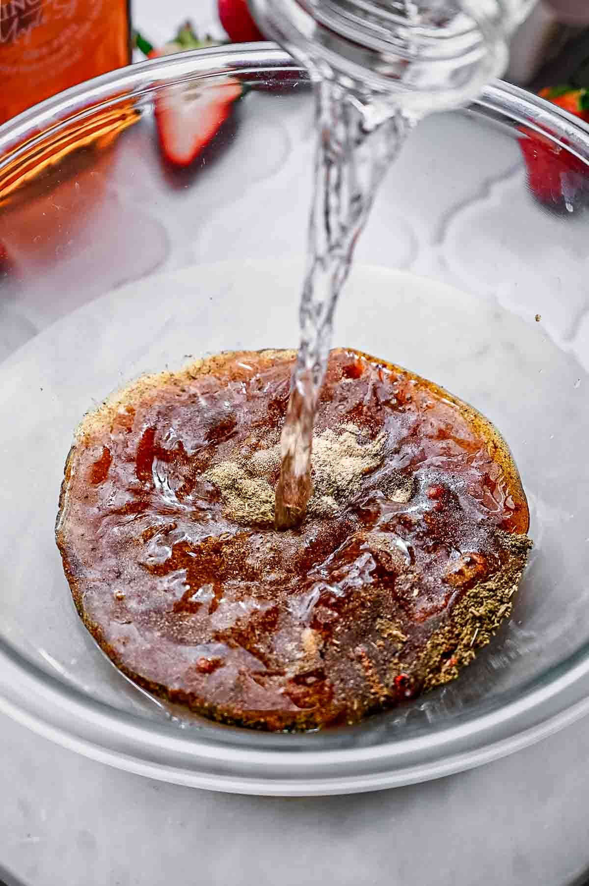 A glass bowl filled with spices, soy sauce, oil and water.