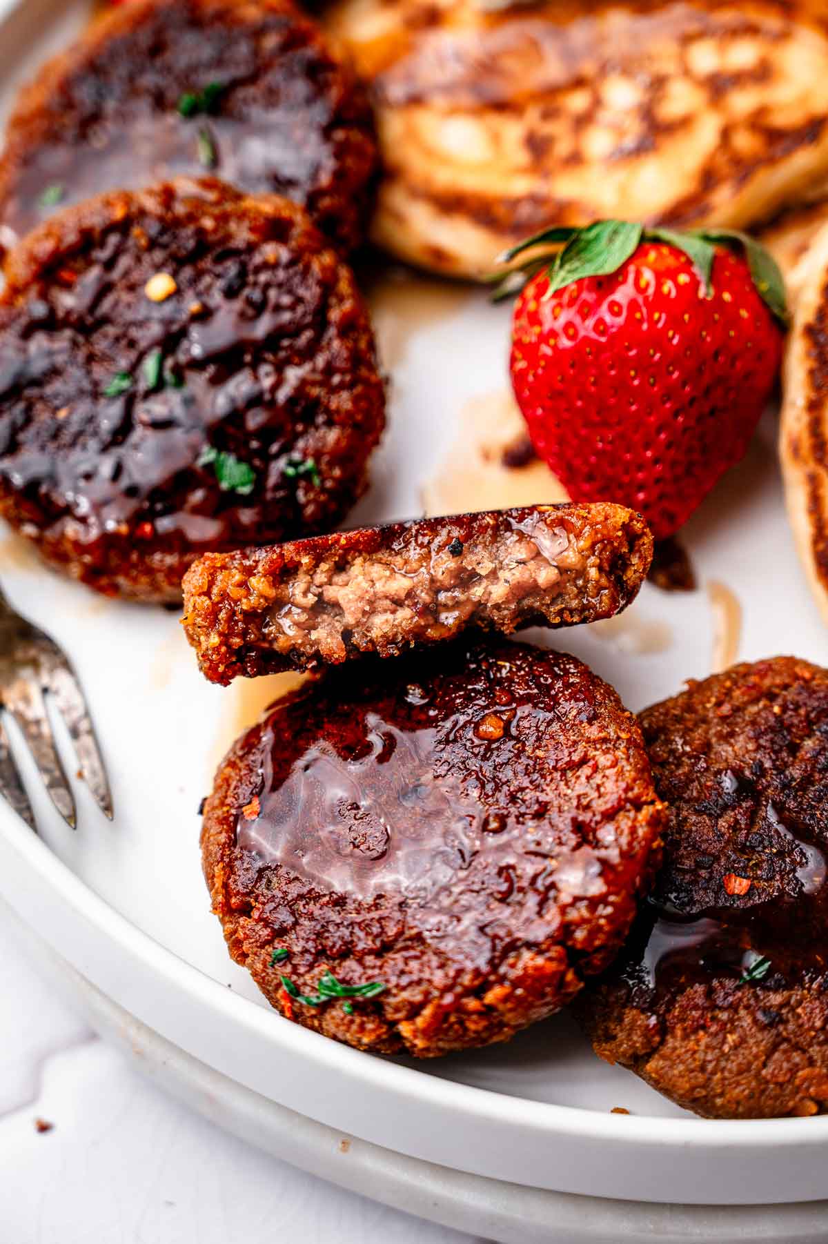 meaty vegan sausage patties on a plate with strawberries and pancakes.