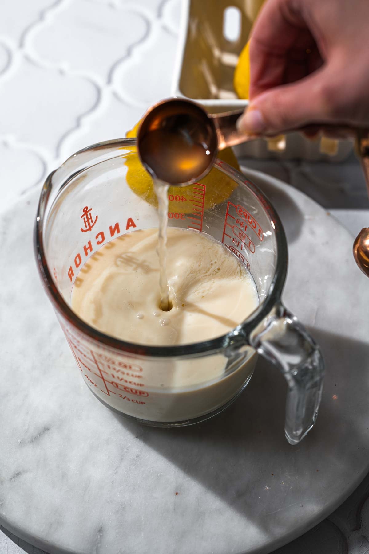 a hand pouring lemon juice into a measuring up with soy milk.