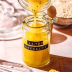 a hand pouring mixed lemon dressing into a glass jar with a vintage label.