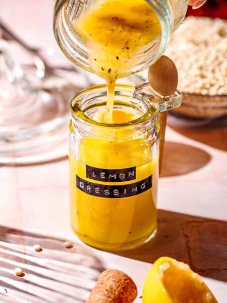a hand pouring mixed lemon dressing into a glass jar with a vintage label.