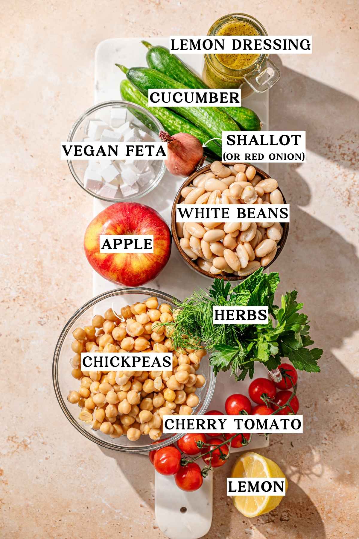 ingredients like white beans, chickpeas, cucumber and vegan feta on a marble tray.