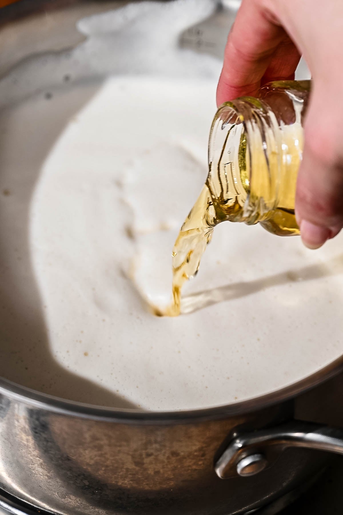 a hand pouring apple cider vinegar into the soy milk mixture.