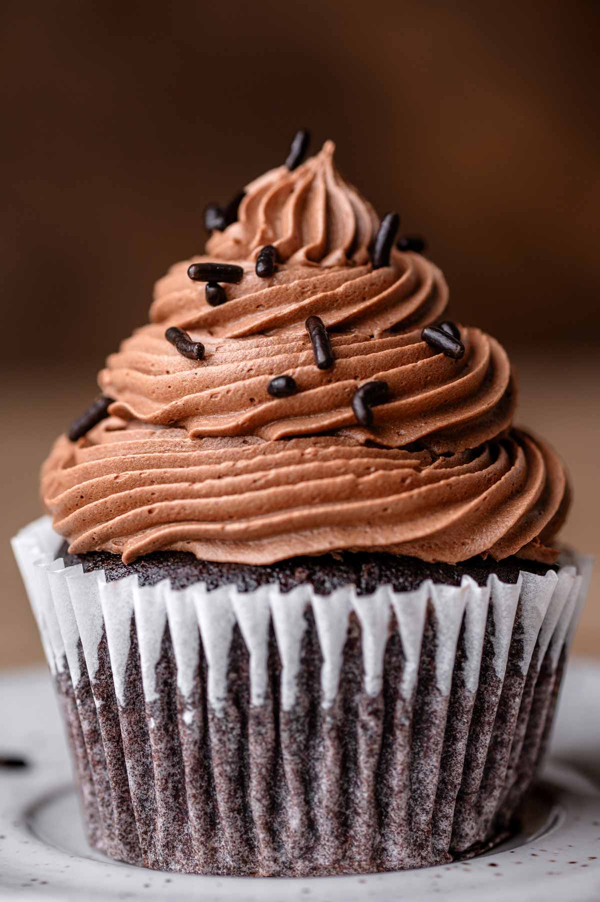 the vegan chocolate frosting piped on a chocolate cupcake with chocolate sprinkles.