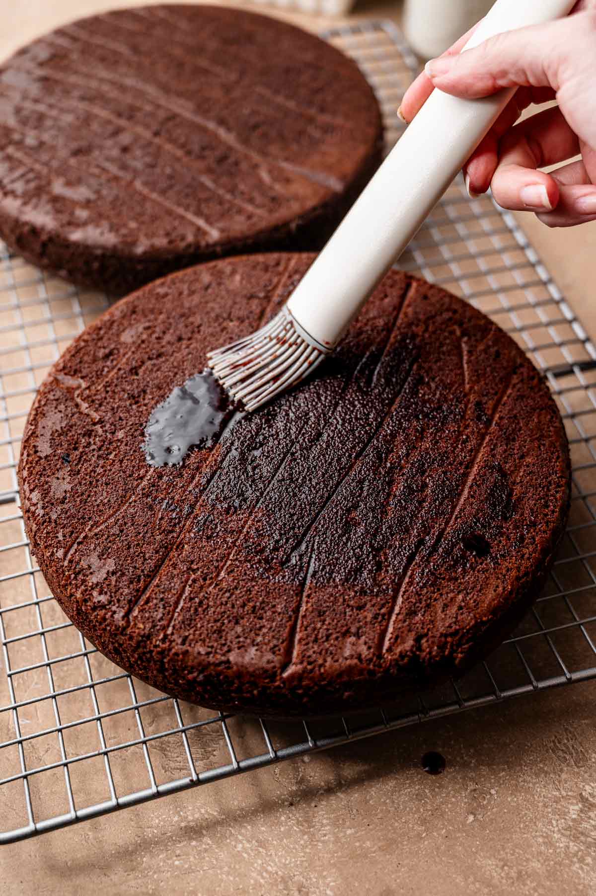 a hand brushing an espresso brown sugar syrup on the cooled cake layer.