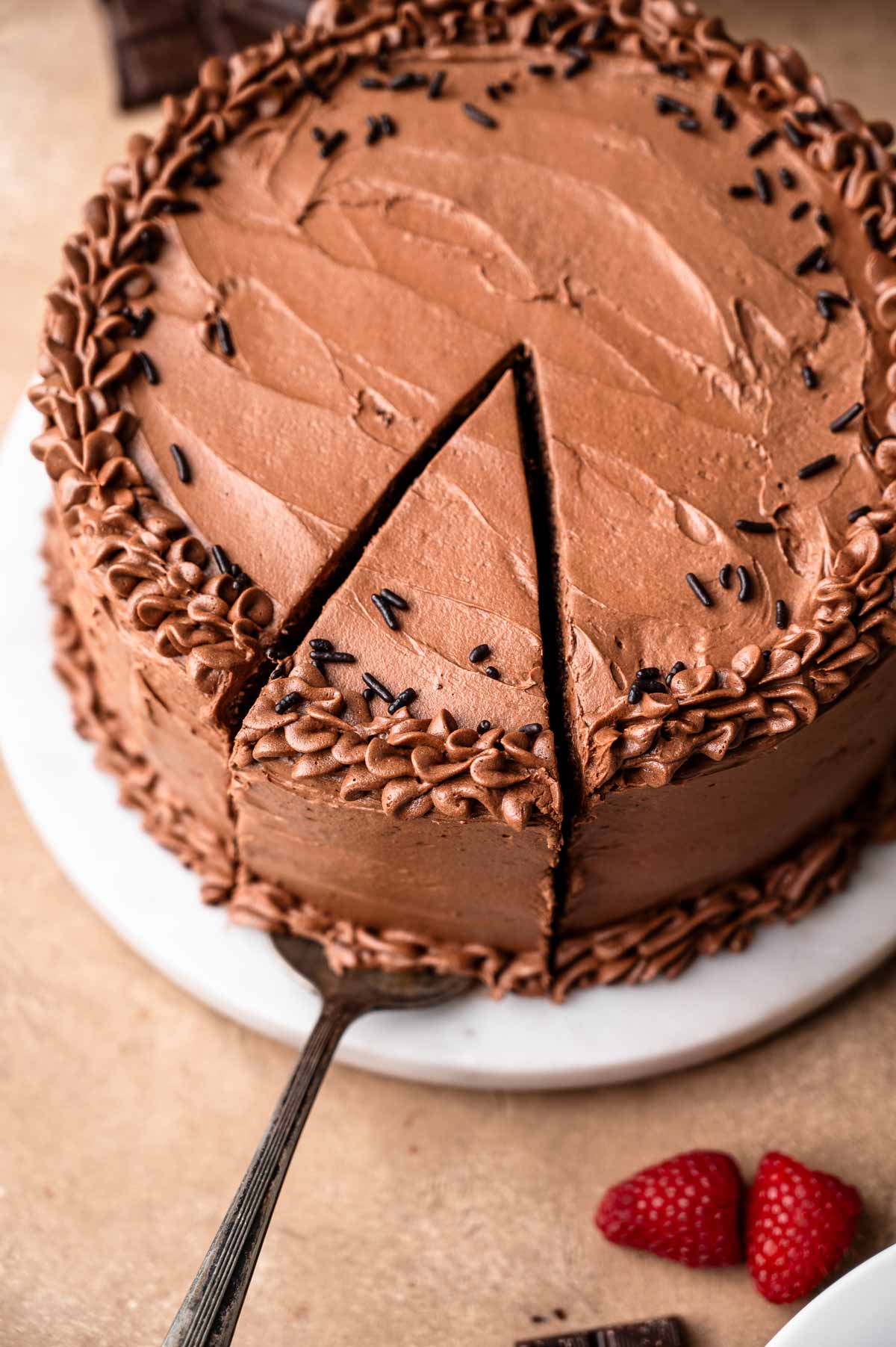 a decorated vegan chocolate cake with a slice being removed by a vintage silver spatula.