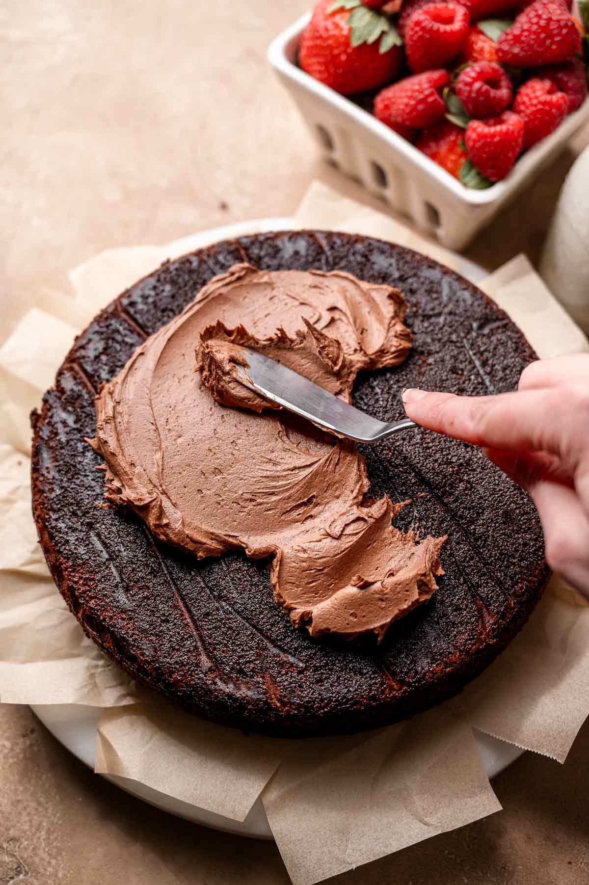 a hand spreading vegan chocolate buttercream on a cake layer.