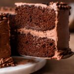 a slice of vegan chocolate cake on a spatula being lifted off a cake tray.