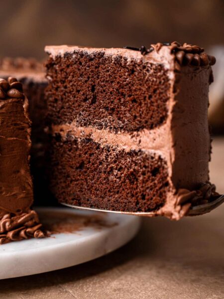a slice of vegan chocolate cake on a spatula being lifted off a cake tray.