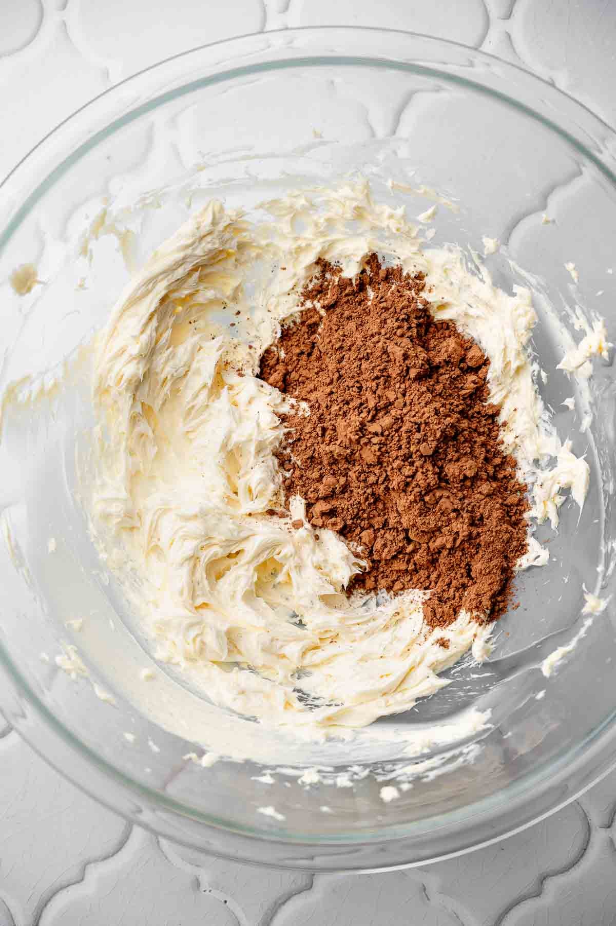 creamed dairy-free butter in a large glass bowl with cocoa powder on top.