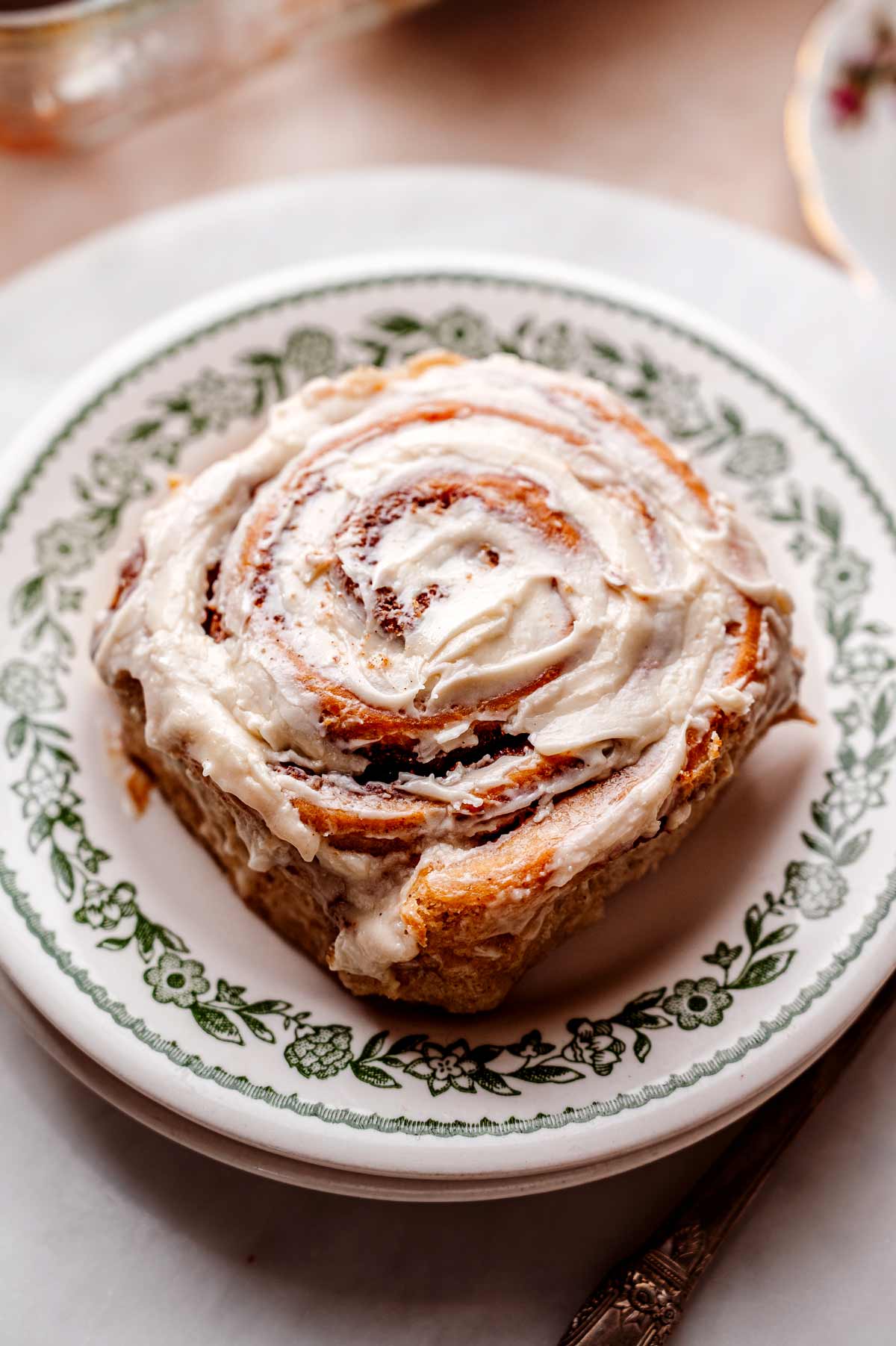 Vegan cinnamon bun with cream cheese icing on a vintage green plate.