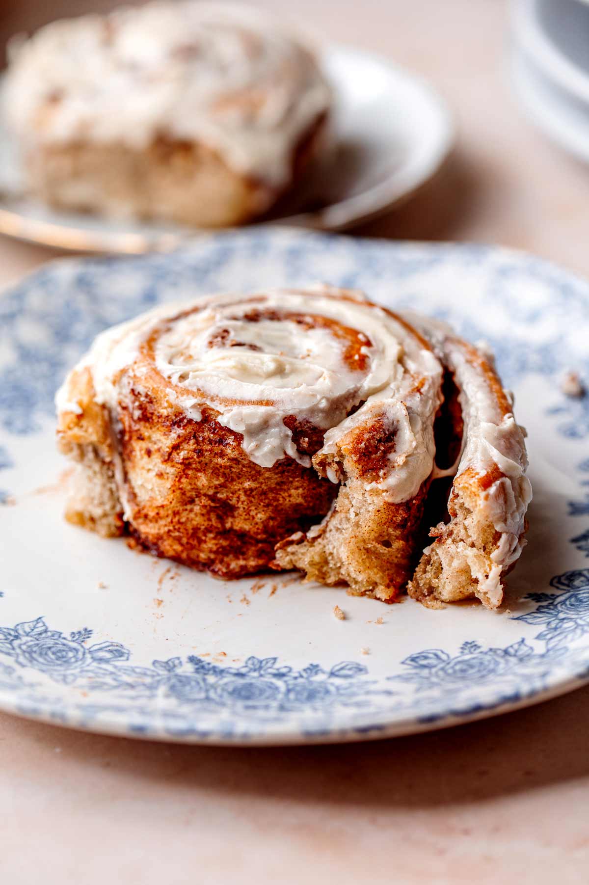 a vegan cinnamon bun that is half eaten on a blue vintage plate showing the fluffy dough texture.