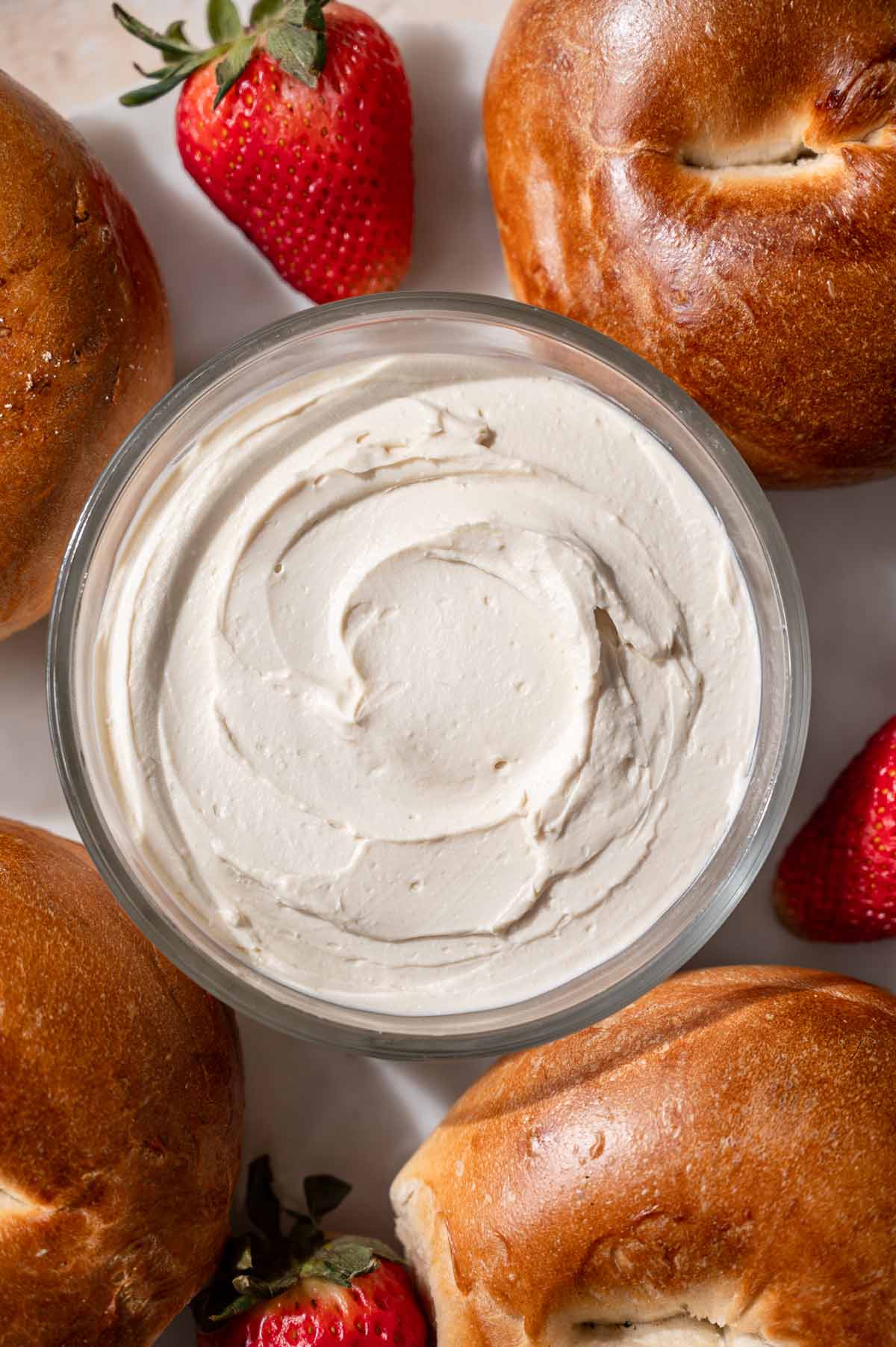 a glass container with homemade vegan cream cheese surrounded by bagels.