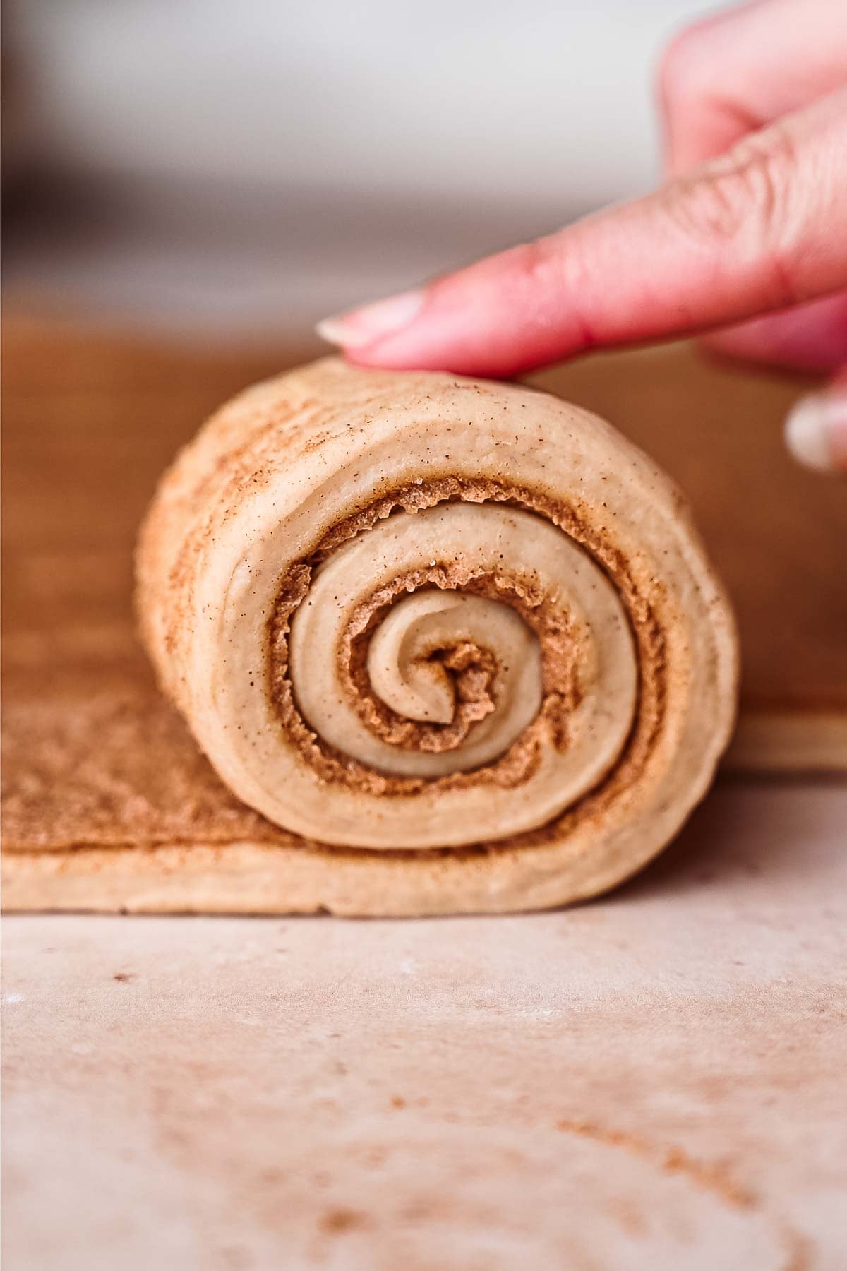 a finger rolling up the cut strips of vegan cinnamon roll dough.