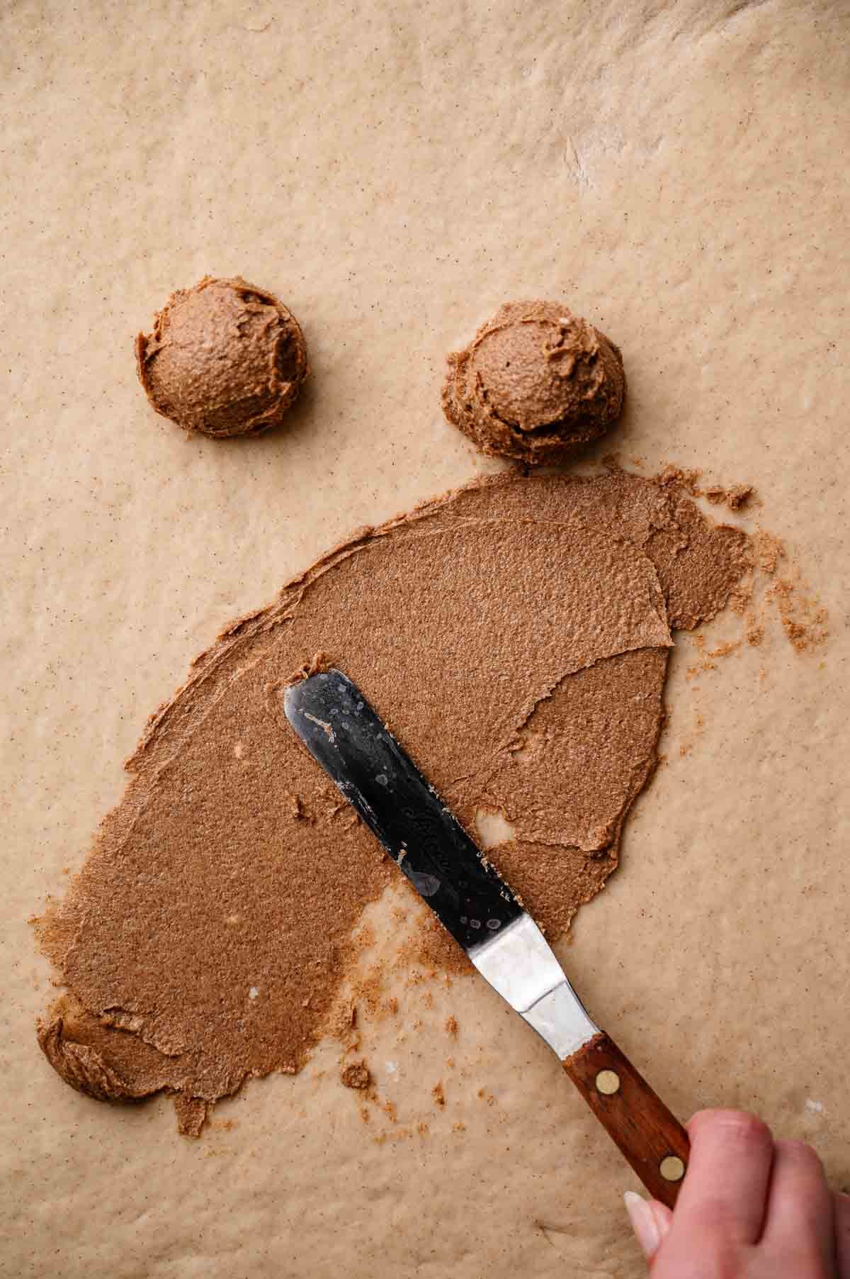 an offset spatula spreading the cinnamon filling onto the rolled out dough.