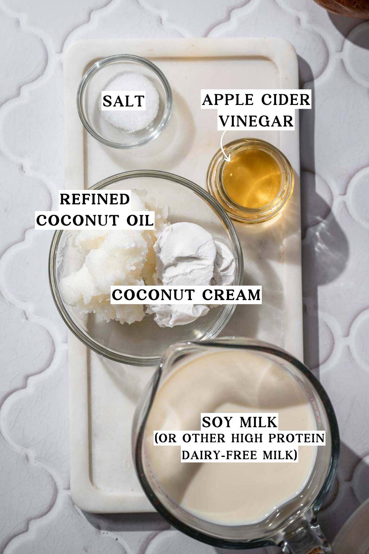 ingredients like soy milk, coconut oil and vinegar on a marble tray.