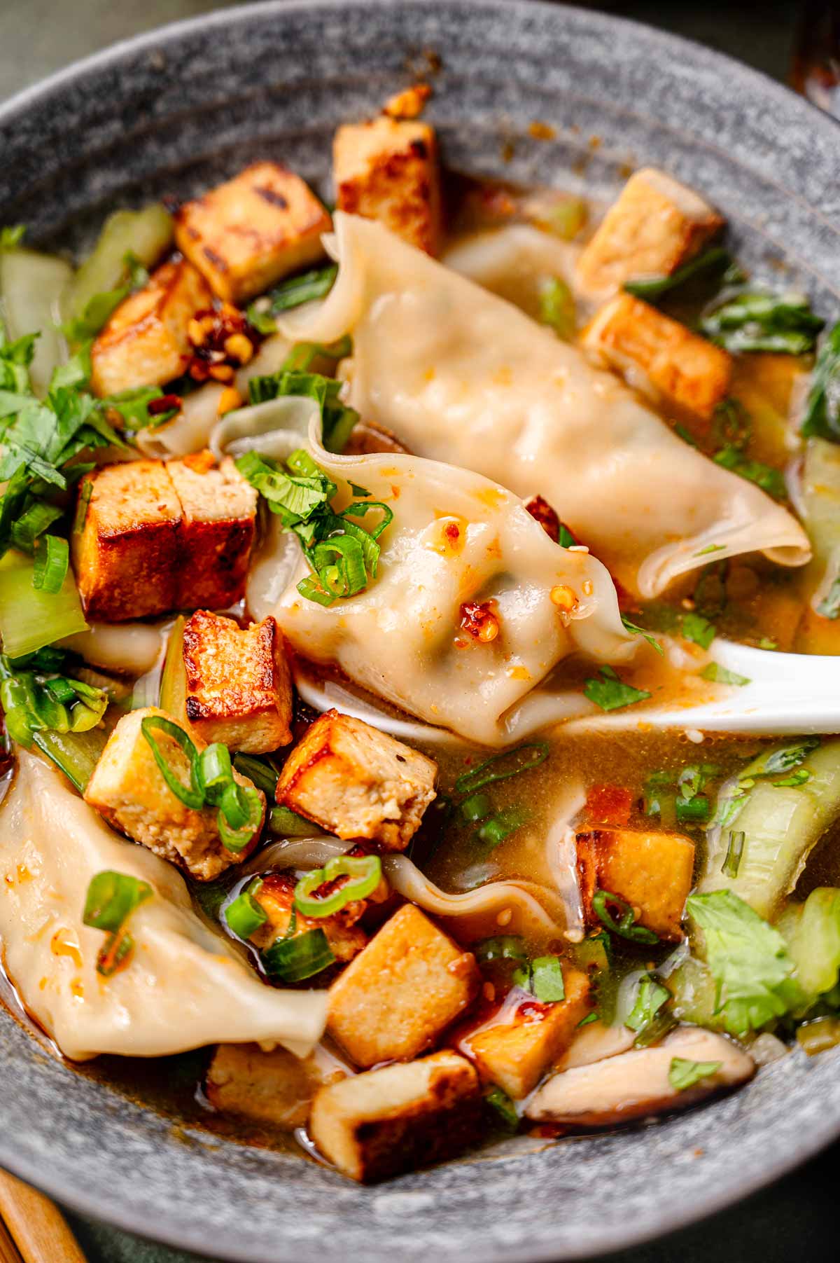 a close up image of a vegetable soup dumpling on a soup spoon surrounded by broth and tofu.