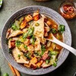 vegan dumpling soup in a grey bowl with a white soup spoon resting on the edge.