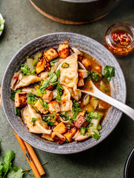 vegan dumpling soup in a grey bowl with a white soup spoon resting on the edge.
