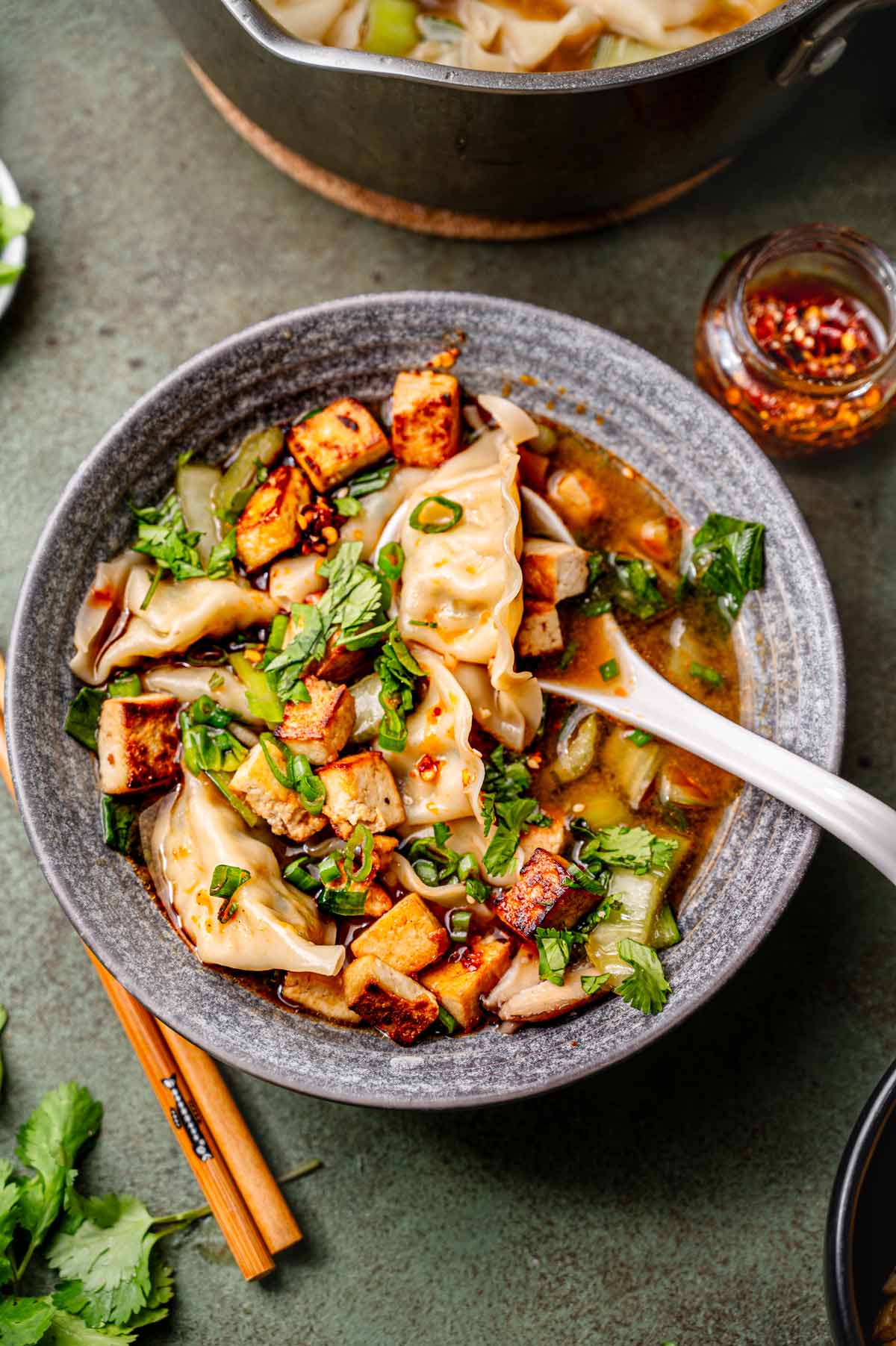 vegan dumpling soup in a grey bowl with a white soup spoon resting on the edge.