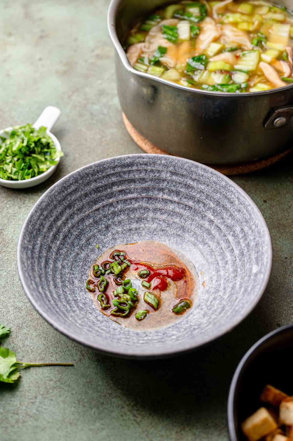 a serving bowl with soy sauce, sesame oil and sriracha in the bottom.