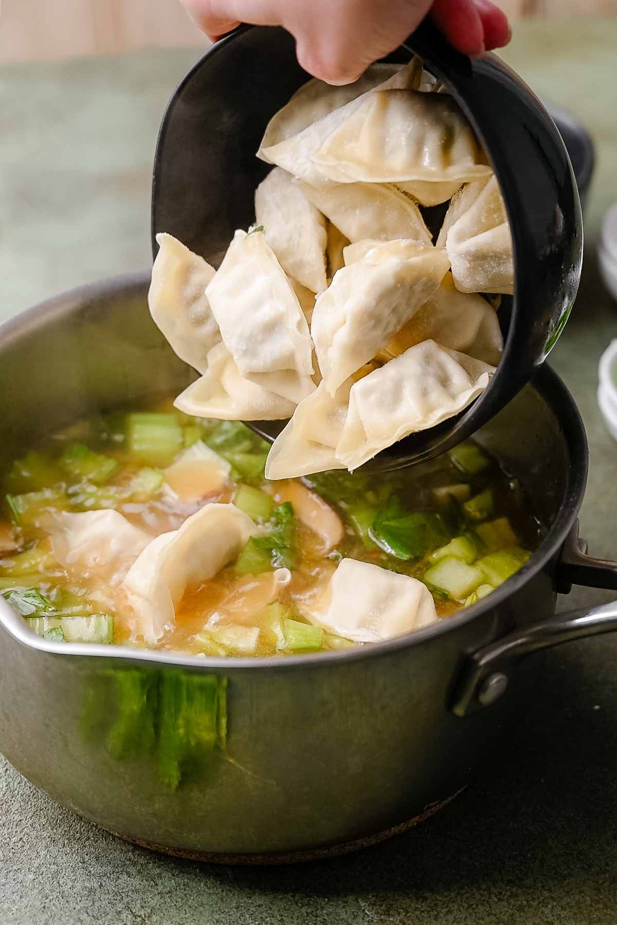 a hand pouring a bowl of frozen vegetable soup dumplings into the hot broth.