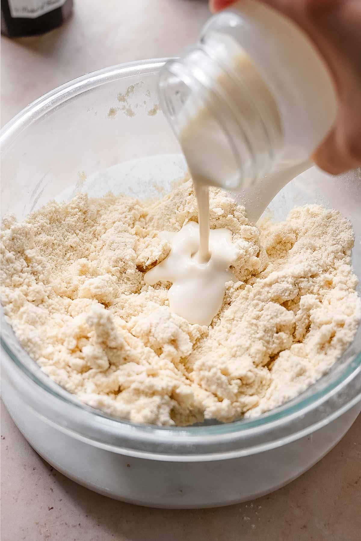a hand pouring vegan buttermilk into the biscuit dough.