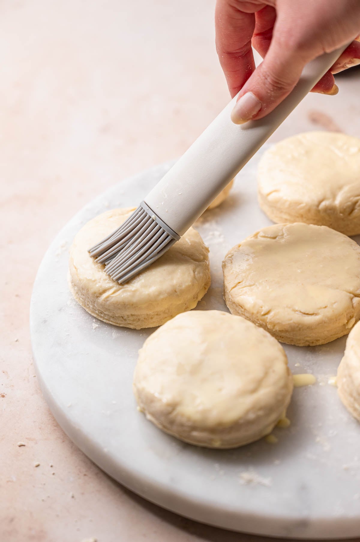 a hand brushing vegan egg wash on the cut out biscuits.