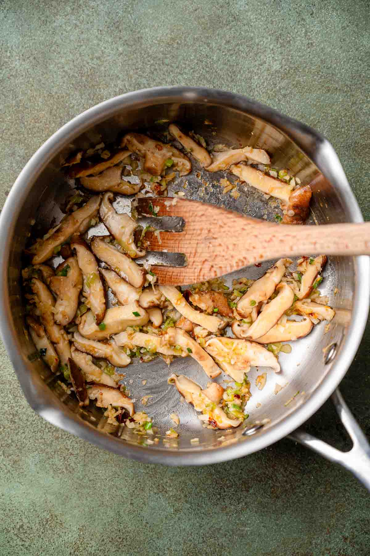 a stainless steel pot with cooked minced garlic, ginger and sliced shiitake mushrooms.