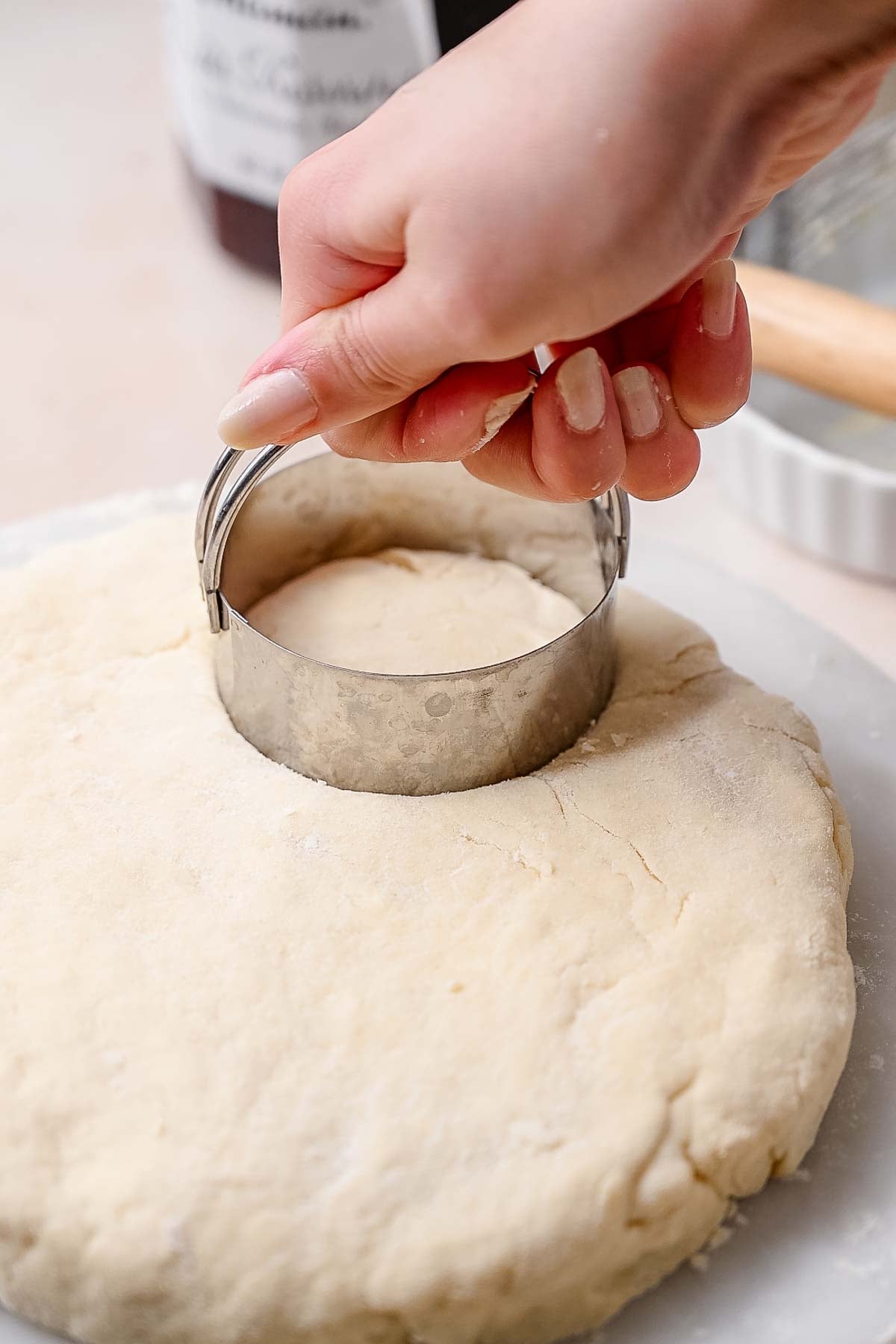a hand using a metal circular cutter to cut out the biscuit dough.